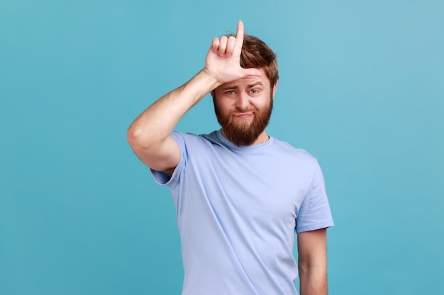 Man in blue Tshirt showing looser gesture holds fingers near forehead sad because of silly mistake