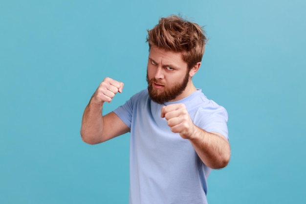 Man in blue Tshirt standing with boxing fists and ready to attack or defence looks with angry face