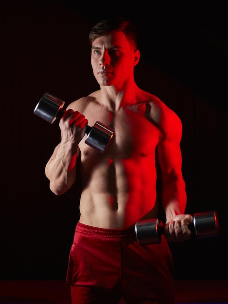 Man bodybuilder lifting dumbbells working focused on his biceps in front of the mirror at the gym Athlete holding two dumbbells showing straining veins on hands bubble guts