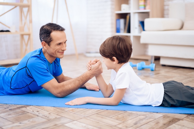 The man and the boy are engaged in arm-wrestling.