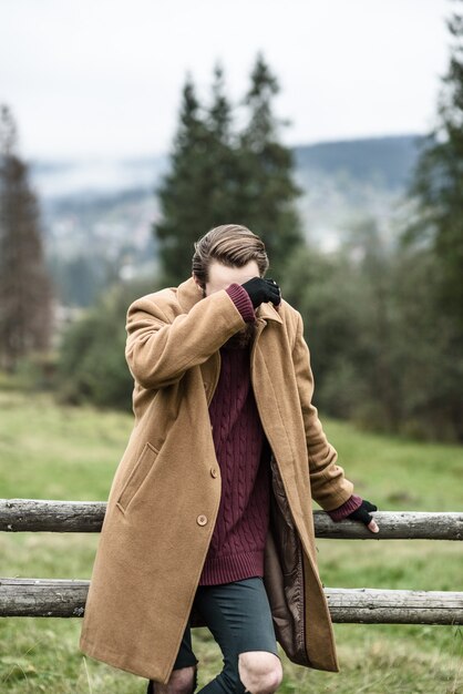 Man in a brown coat and torn trousers was leaning against the fence