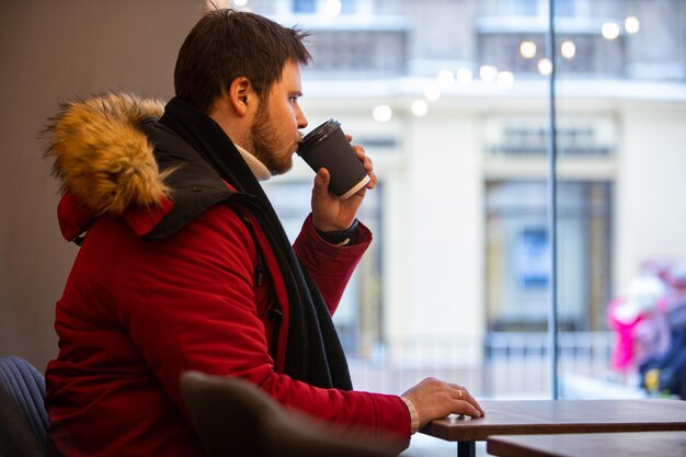 man in cafe in red winter coat drinking tea warming up inside