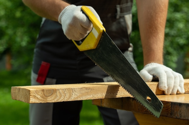 Man carpenter saws a wooden board with a hand saw