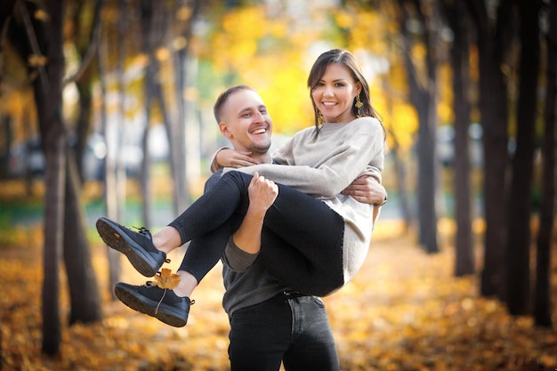 A man carries a woman in his arms in the autumn park a happy couple spend time together