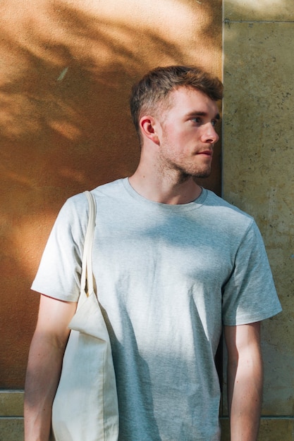 Man carrying cloth bag and standing near wall looking away