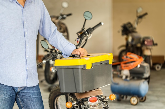 Man carrying toolbox in repair shop Mechanic repairing motorcycle in workshop garage Repairing and maintenance concepts