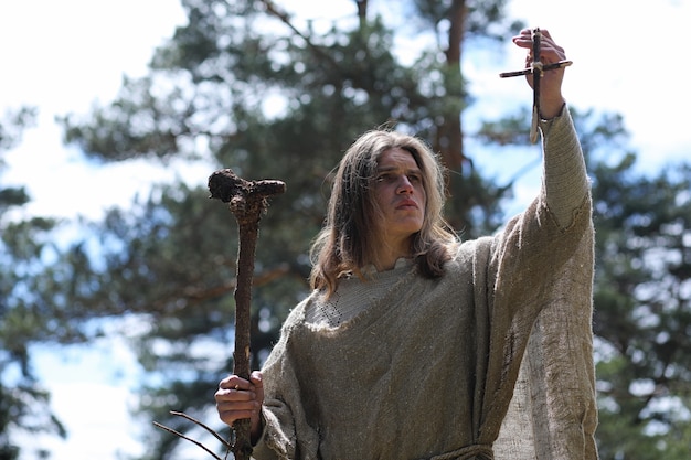 A man in a cassock spends a ritual in a dark forest with a crystal ball and book