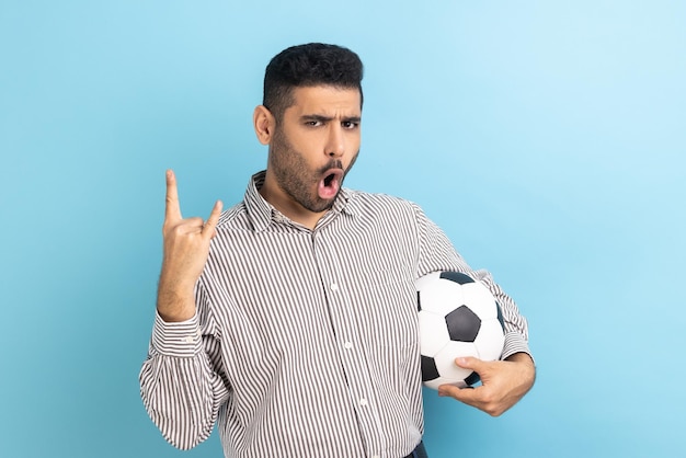 Man celebrating victory of favourite football team holding soccer ball in hands showing rock gesture