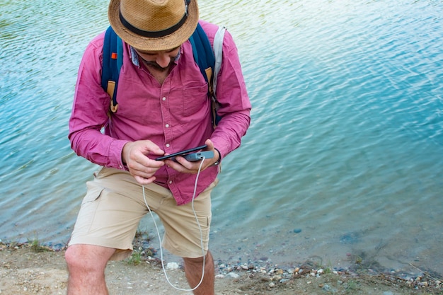 Man charges a smartphone with a portable charger. A man with a power bank in his hand on the background of the sea on a bright sunny day with clouds.