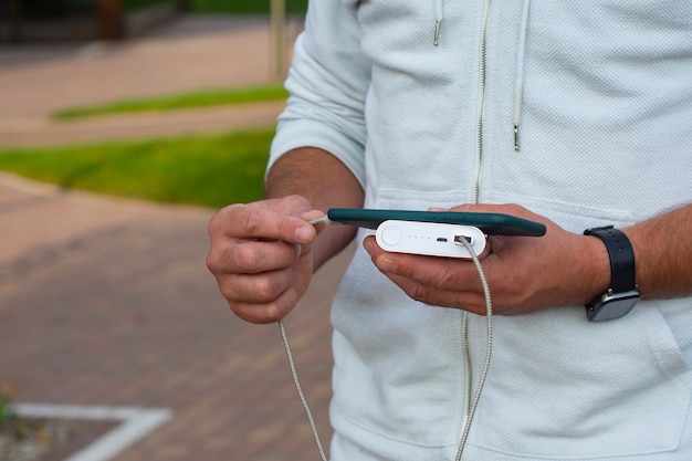 Man charges a smartphone with a power bank in hand. Portable charger for charging gadgets.