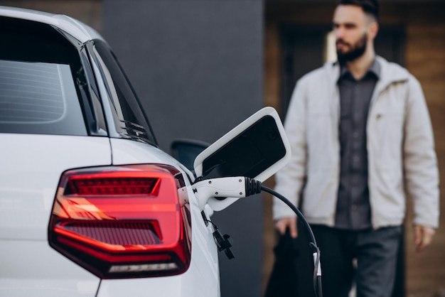 Man charging electric car by the house