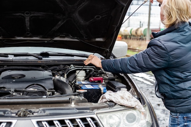 A man checks the oil level in a car engine with an iron dipstick Technical check of the car