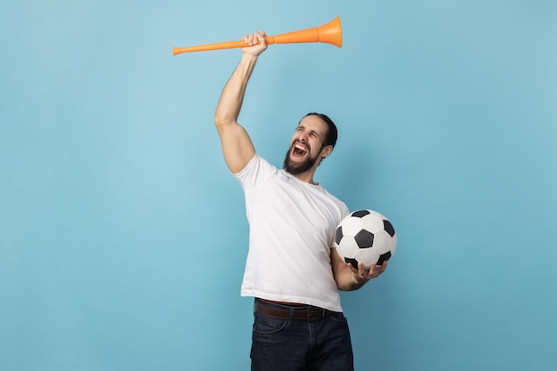 Man cheering for favorite football team holding horn and ball in hands looking screaming happily