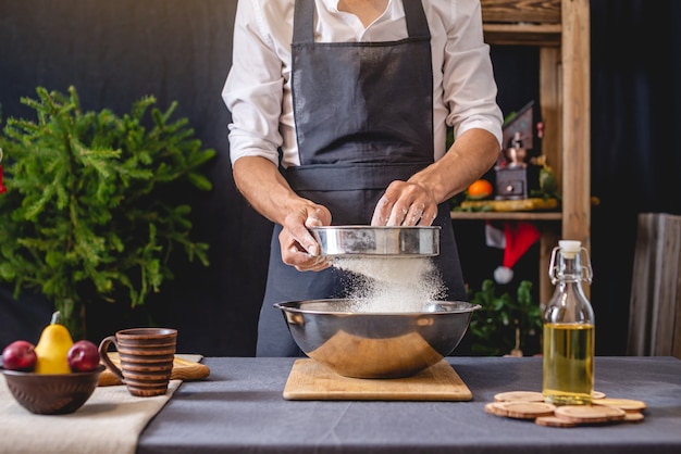 Man chef in a black apron kneading the dough with his hands for Christmas baking