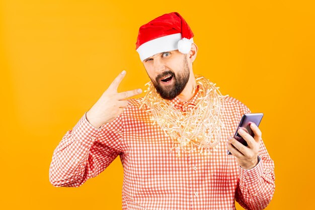 A man in a Christmas hat of Santa Claus, a red plaid shirt and a garland around his neck poses for the camera