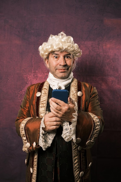 Man in classic medieval clothes looking at camera while using a mobile phone over an isolated background.