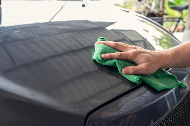 Man cleaning car with green microfiber cloth on hood