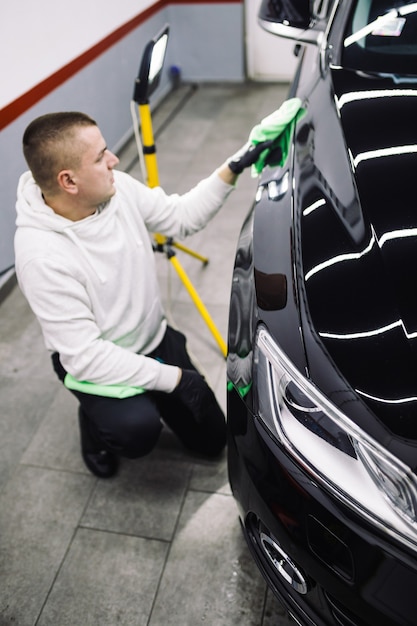 A man cleaning car with microfiber cloth, car detailing (or valeting) concept. Selective focus.