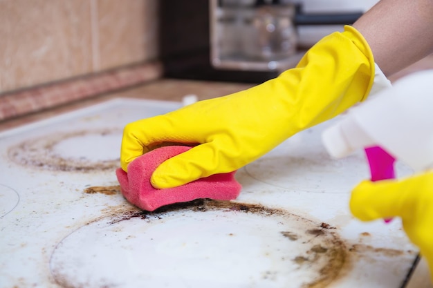 Man cleaning ceramic modern stove or hob with detergent agent Hand in yellow gloves clean stove from burnt and grease dirt Housework professional cleaning service after tenants