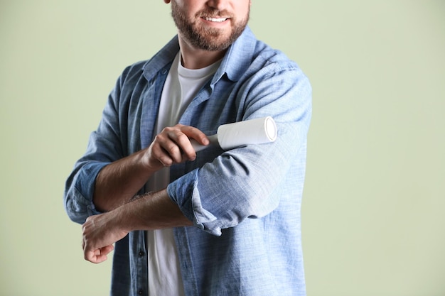 Man cleaning clothes with lint roller on light background closeup