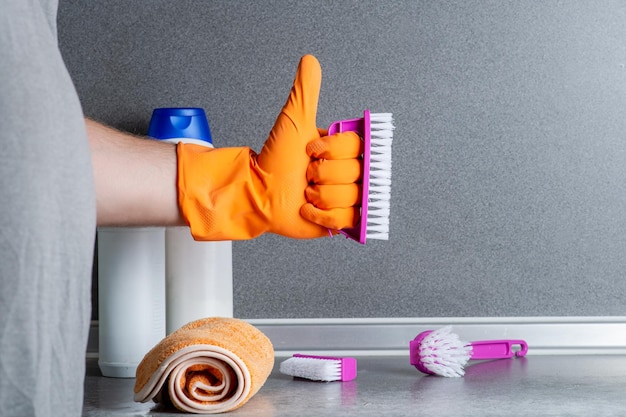 Man and cleaning concept A man's hand holds an approving gesture with a hand in a rubber glove against the background of cleaning products on the kitchen table