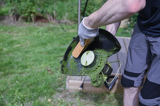 man cleaning a electric trimmer from grass after work with a brush gardening concept