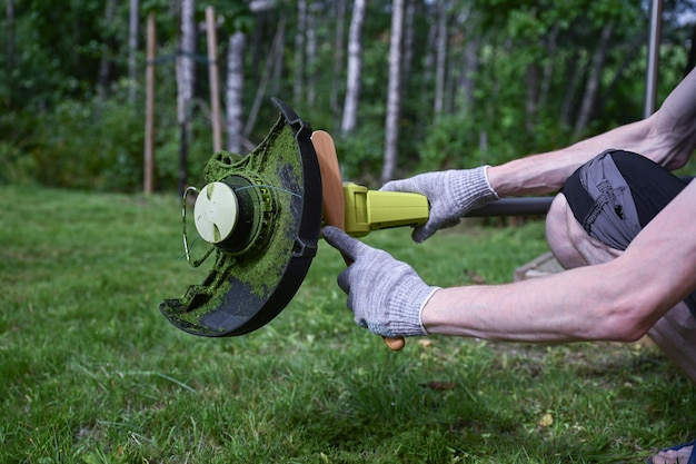 Photo man cleaning a electric trimmer from grass after work with a brush gardening concept