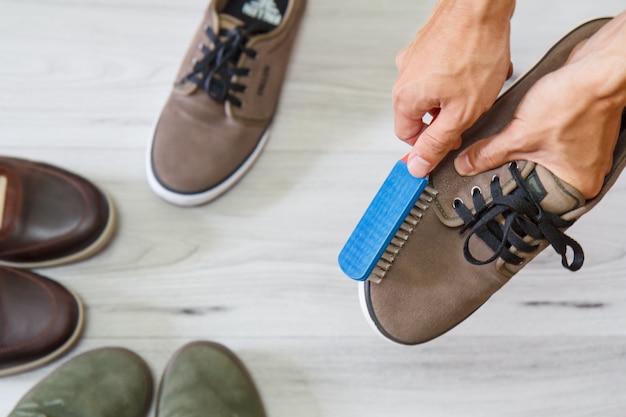 Photo man cleaning and polishing leather shoes with brush on wooden background