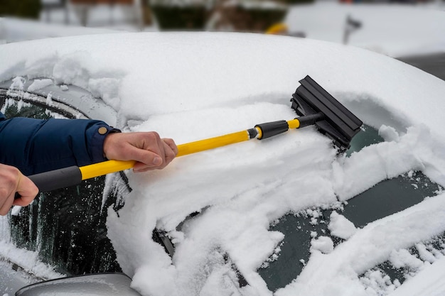 Man cleaning snow off his car during winter snowfall