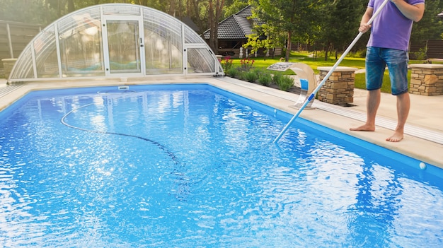 Man cleaning swimming pool with vacuum tube cleaner early