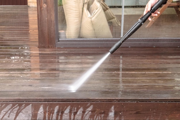 Man cleaning walls and floor with high pressure power washer Washing terrace wood planks and cladding walls