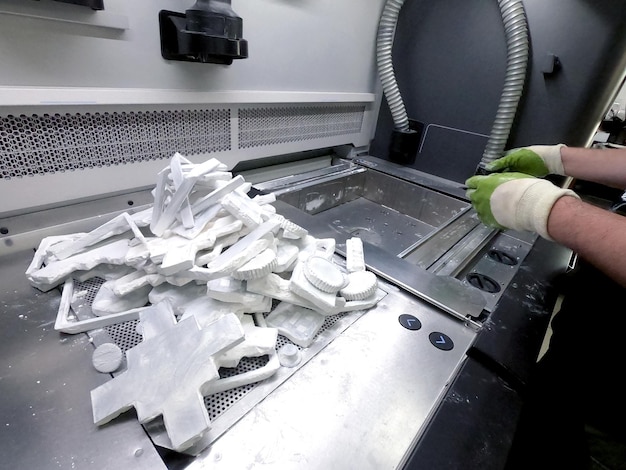 Man cleans details printed on industrial 3D printer from white plastic powder