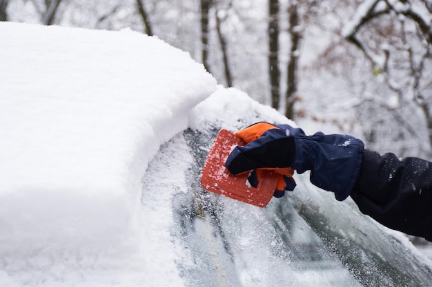 Man cleans his car after a snowfall Cleaning snow from windshield Scraping ice Winter car window cleaning