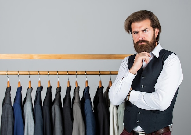 Man clothing in boutique Man with suit tailor in his workshop Handsome bearded fashion man in classical costume suit Man in custom tailored suit presenting expensive tuxedo Another client