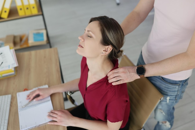 Man colleague massages shoulders of tired woman with hands