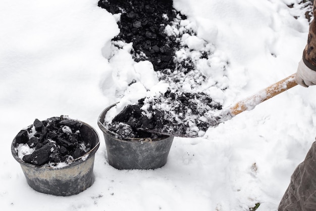 A man collects coal from under the snow with a shovel into buckets heating of a residential building