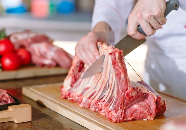 A man cook cuts meat with a knife in a restaurant.