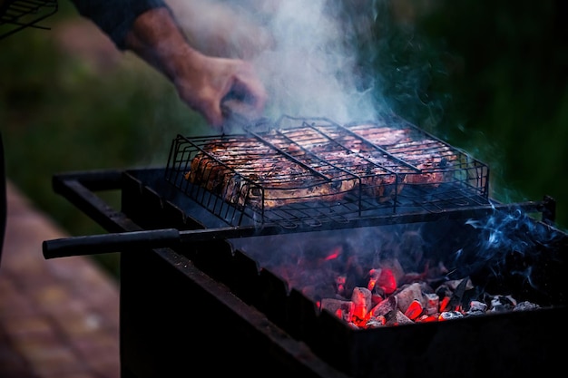 a man cooks meat on a grill in which coals burn in nature