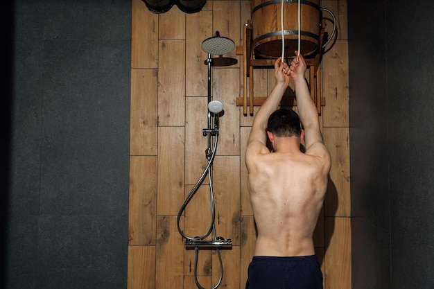 Man cools off after a hot sauna using a wooden waterfall bucket as a contrast shower