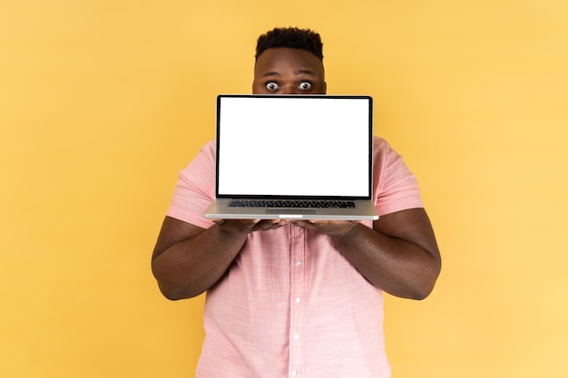 Man covering half of face with laptop with blank white screen and looking at camera with big eyes