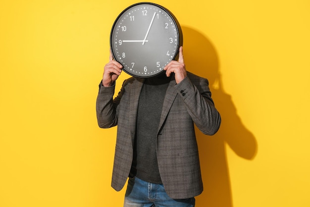 Man covering his face with big clock on yellow background