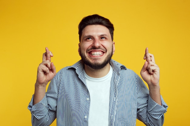 Man crosses fingers, dressed in casual clothes, isolated over orange background