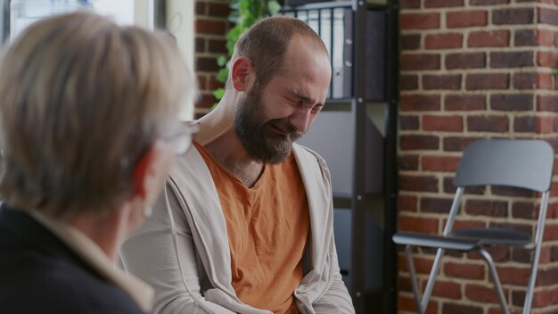 Photo man crying in front of psychologist because of addiction and depression at aa therapy meeting. desperate adult having mental breakdown and anxiety at support group session with people.