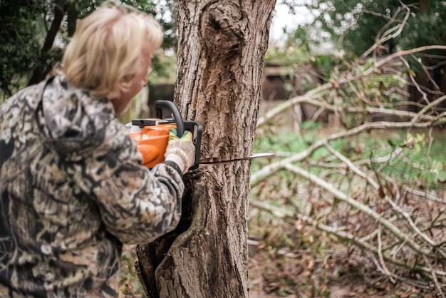 A man cuts down an old tree with a chainsaw. Removing old plants in the garden.