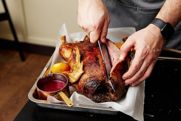 Man cuts duck baked with orange fruits at table closeup