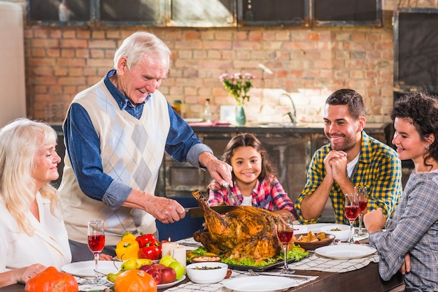 Man cutting baked chicken at table with family 