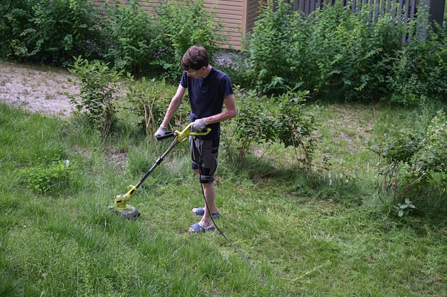 Photo man cutting grass in the lawn with an electric trimmer