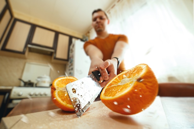 Man cutting juicy orange in half with splashes in kitchen