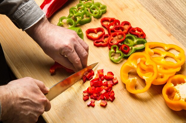 Photo man cutting red bell pepper on a wooden kitchen board