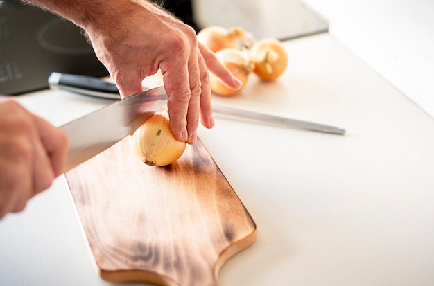 Man cutting white onion with knife, only hands